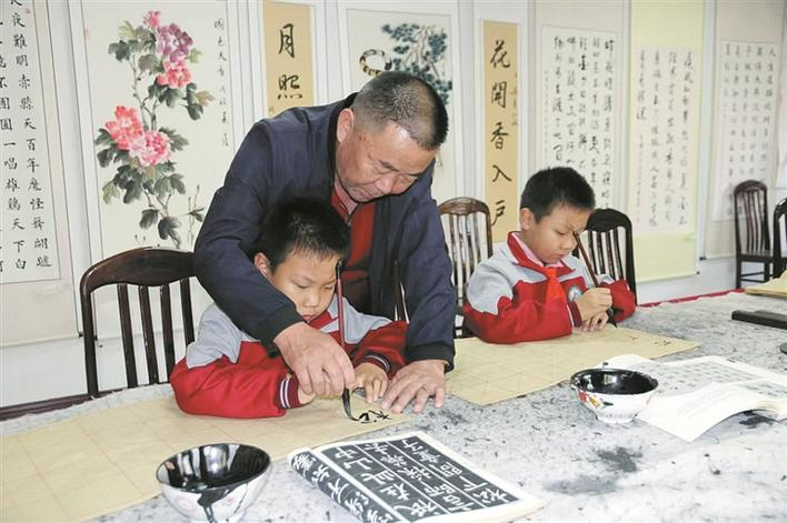 刘广义（中）在教孩子们练习书法（资料图片）。张梅英 潘彩兰 摄